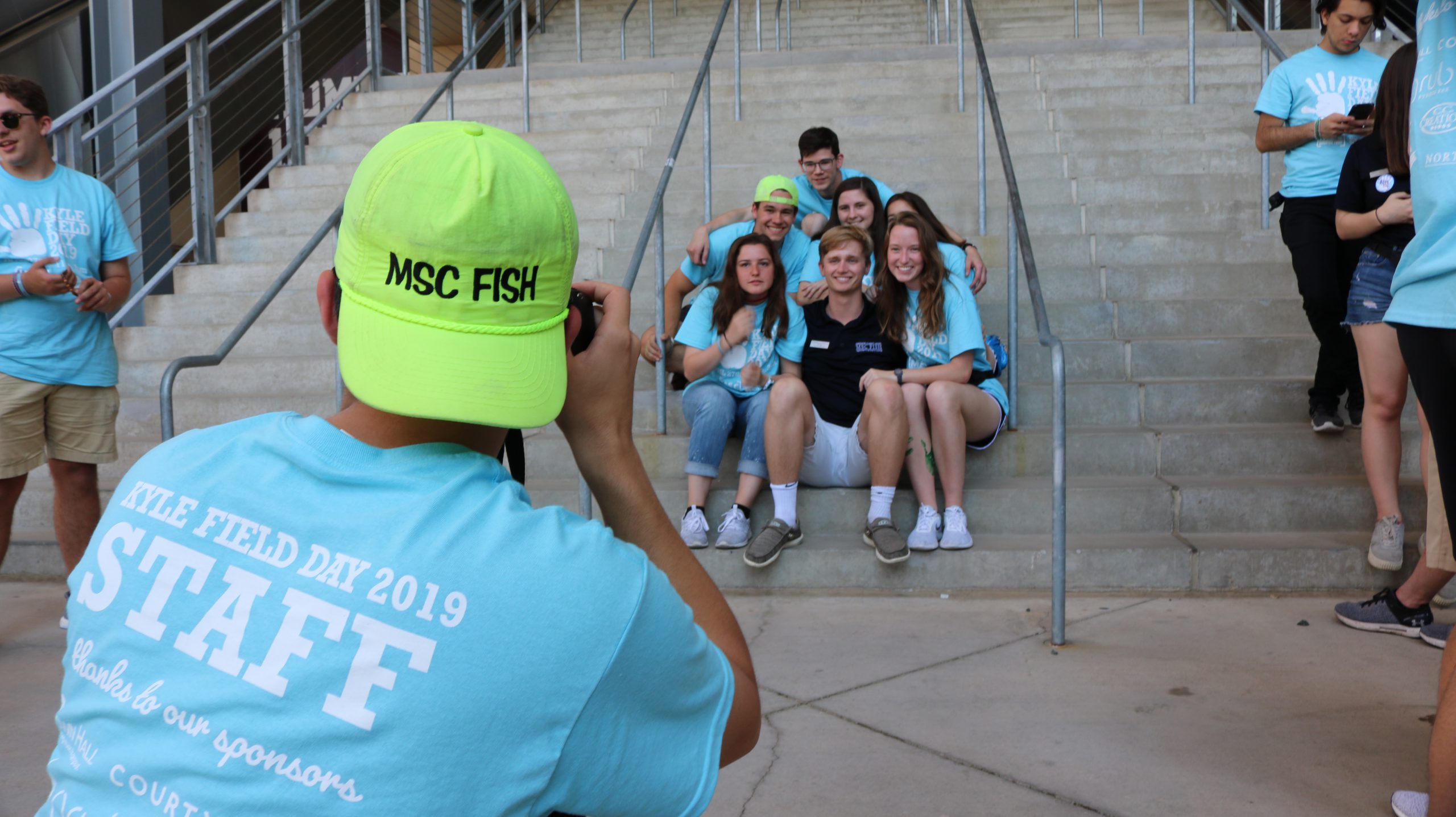 MSC FISH member taking a picture of a group of other MSC FISH members sitting and posing inside of Kyle Field at the Kyle Field Day event